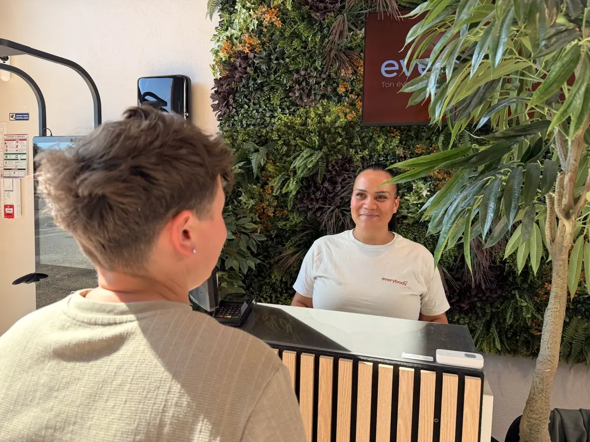 La coach vous accueille au comptoir, sourire et mur végétal