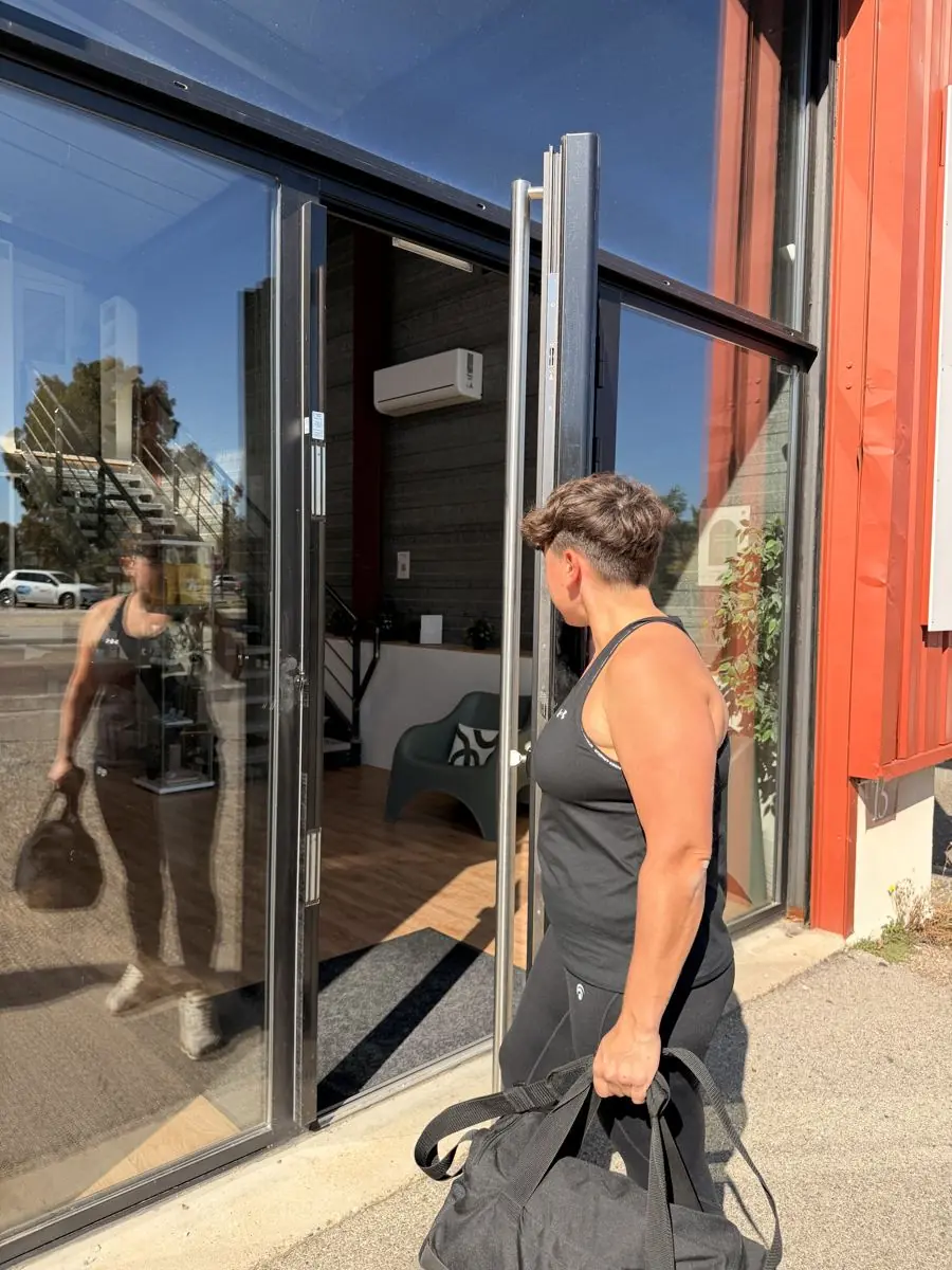 Une adhérente pousse la porte du studio EVERYBODYFIT, sac de sport à la main